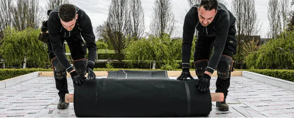 Twee dakdekkers die EPDM dakbedekking aan het uitrollen zijn op een plat dak