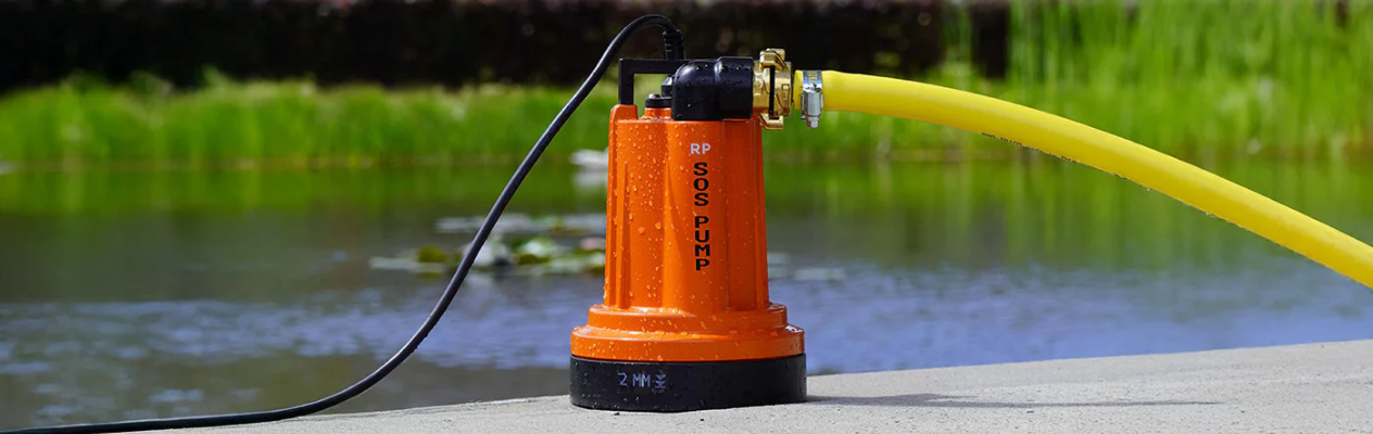 Oranje SOS-PUMP® vlakzuigende dompelpomp met gele slang, in gebruik bij vijver of regenwaterput.